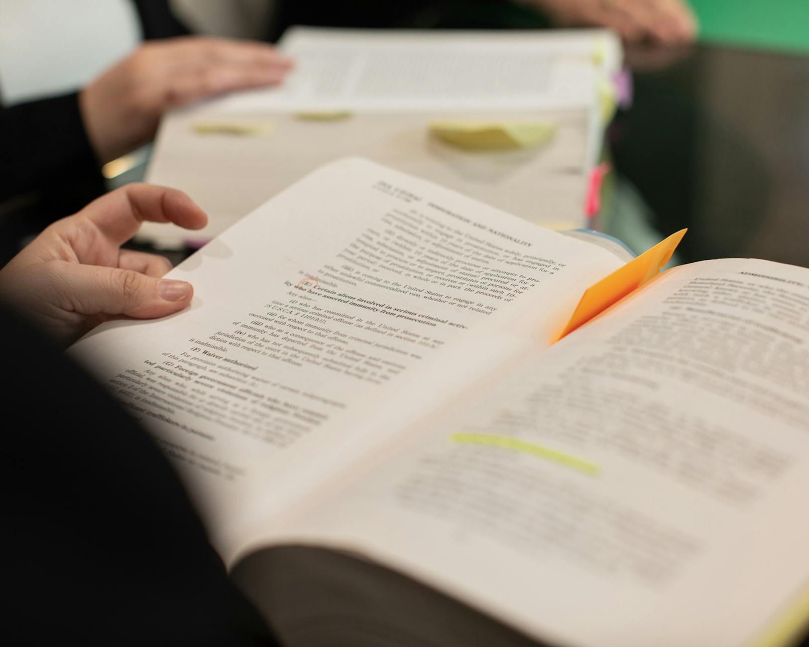 Osoba sústredene číta knihu pri stole s poznámkami
